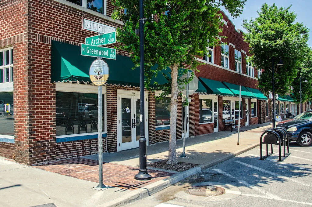 The corner of N. Greenwood Avenue and E. Archer Street, with brick storefronts, green awnings, and the Black Wall Street historical marker