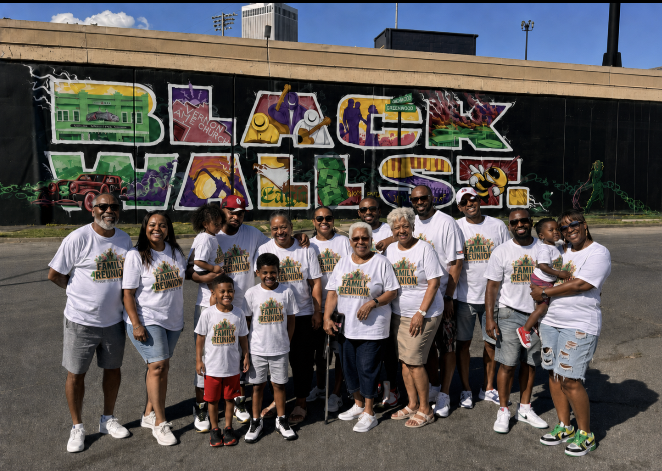 A multi-generational family in matching Family Reunion t-shirts posing in front of a Black Wall St. mural in Greenwood
